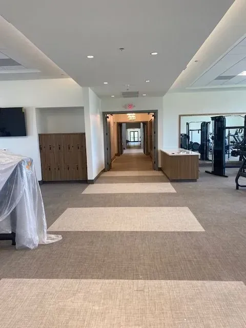 Modern office corridor with carpet tiles, lockers, and gym equipment visible in the distance