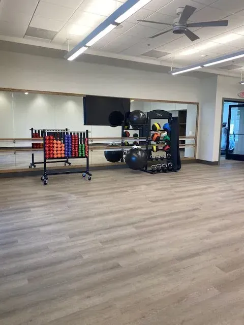 Spacious fitness studio with gray floors, ceiling fans, equipment racks, and exercise balls