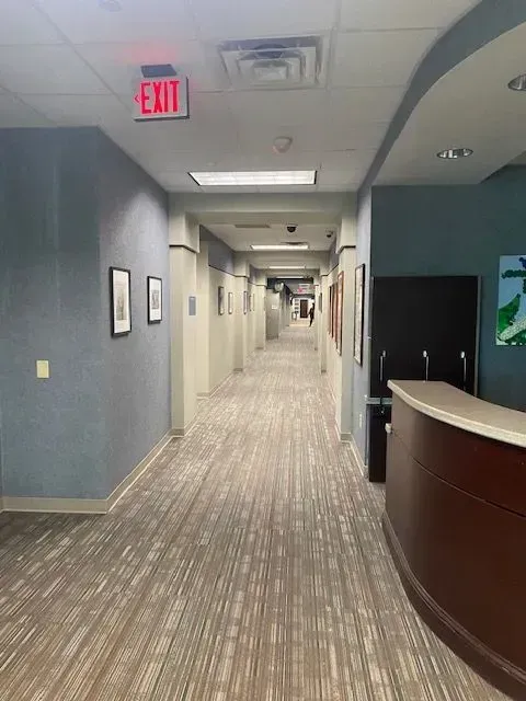 Office hallway with patterned carpet, blue walls, exit sign, and curved reception desk on the right