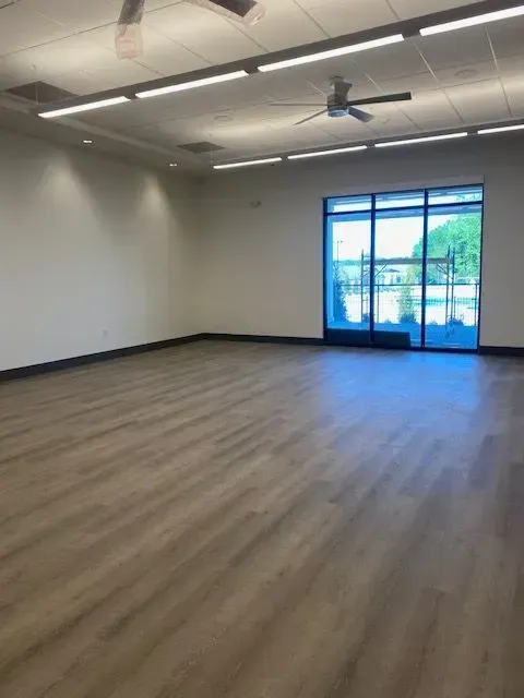 Empty modern room with wood-look flooring, white walls, ceiling fan, and large glass doors to a balcony.