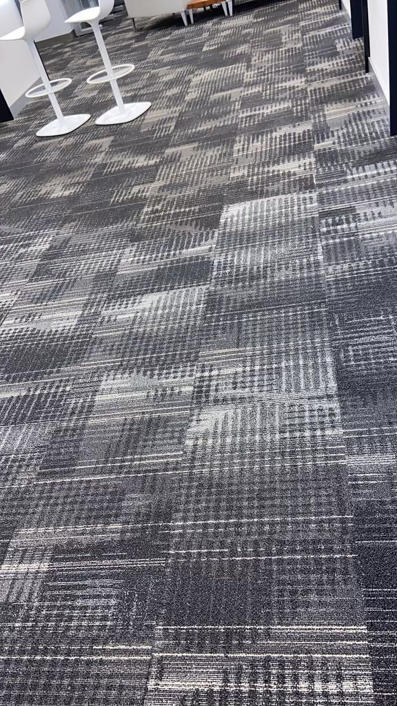 Patterned gray carpet in an indoor office or conference area, with white chair legs visible at the top left.