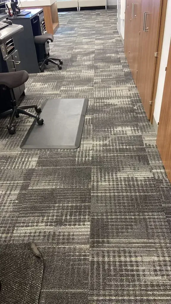 Office hallway with patterned carpet, desks on the left, and wood-paneled walls on the right.
