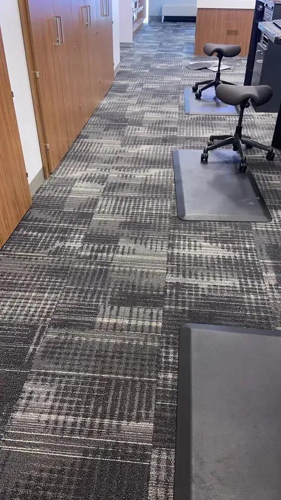 Office hallway with patterned carpet, wooden doors, and rolling chairs on gray mats.