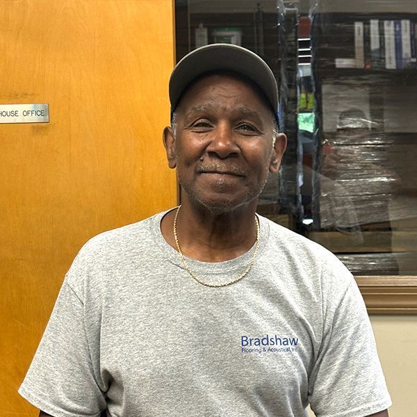 Man standing indoors in a gray shirt and cap, smiling in front of a wooden door.