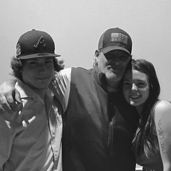 Three people posing together, smiling with arms around each other, in grayscale.