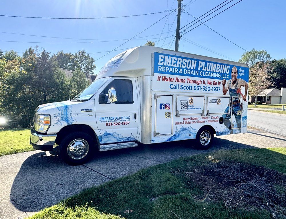 Emerson Plumbing & Heating service truck parked on a sunny roadside with a worker on the side.