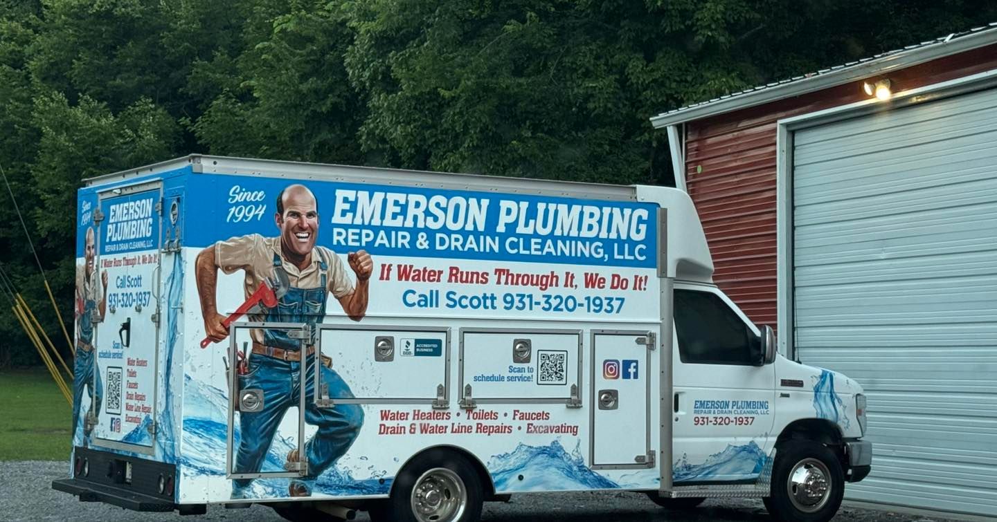 Emerson Plumbing service van parked beside a garage, with blue-and-white company graphics and a plumber illustration