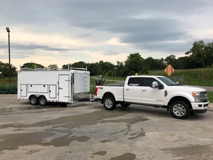 White pickup truck towing a white trailer in a wet parking lot under a cloudy sky