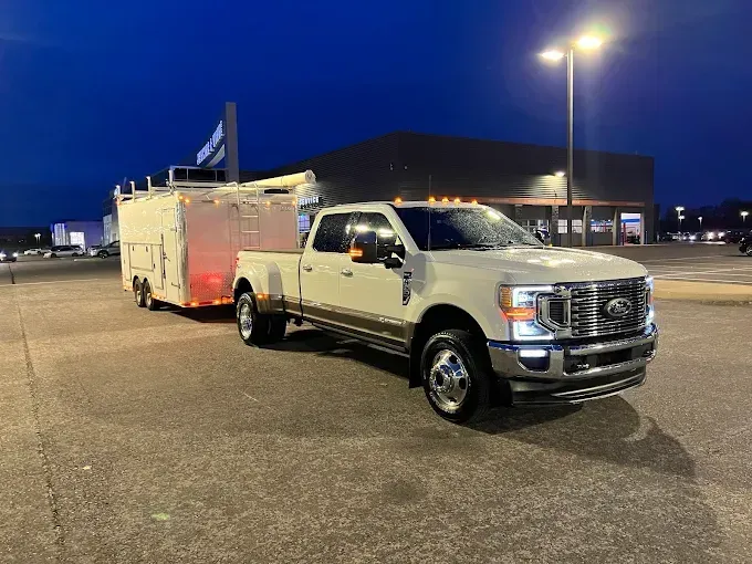 White pickup truck towing a white enclosed trailer in a parking lot at dusk