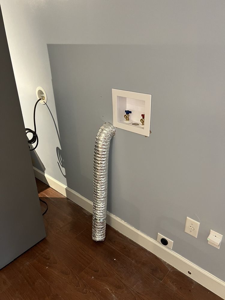 Silver dryer vent hose connected to a wall vent in a gray room with hardwood floor.