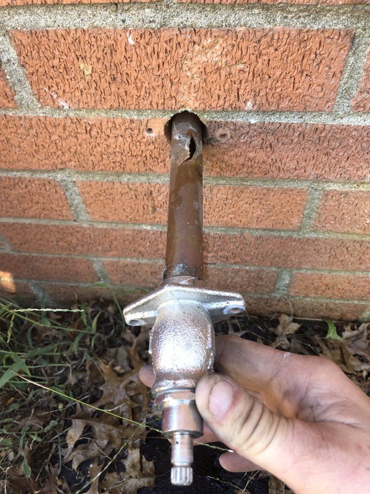 Hand holding a metal hose connector against a brick wall outside