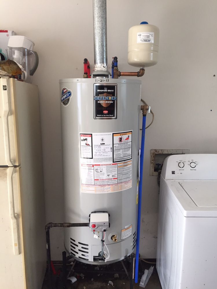Water heater with pipes and expansion tank in a utility room next to a washing machine.
