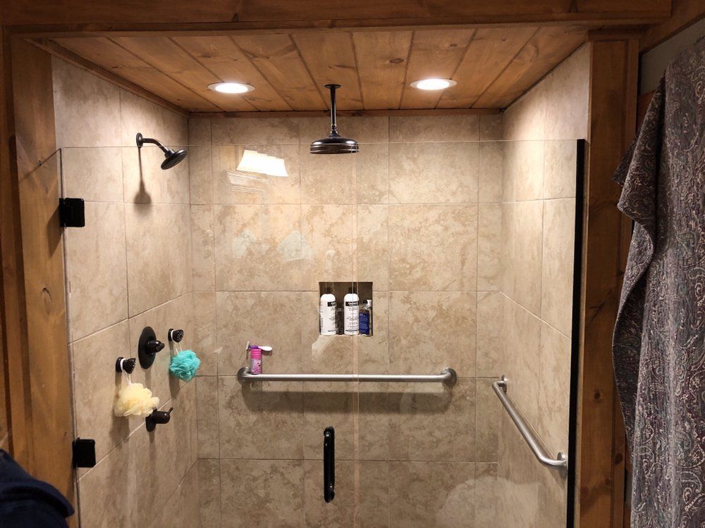 Tile shower stall with a bench, grab bar, and showerheads under warm wood-paneled ceiling lights