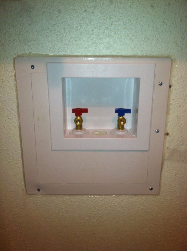 Wall-mounted recessed water supply box with red and blue shutoff valves on a beige wall