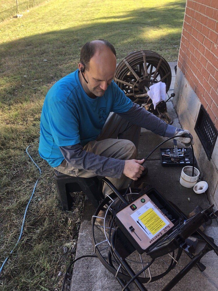 Man working with electronics on a table outdoors beside a brick wall and bicycle wheel