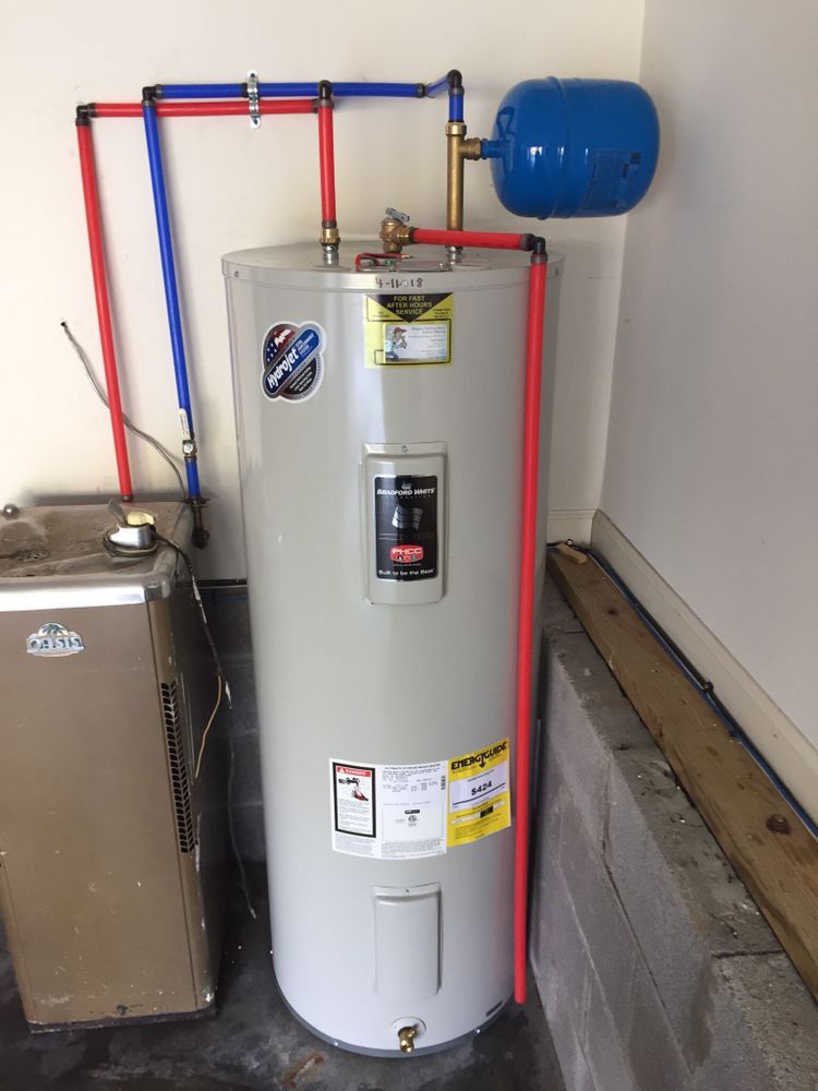 Water heater with red pipes and blue expansion tank beside a small utility sink in a basement.