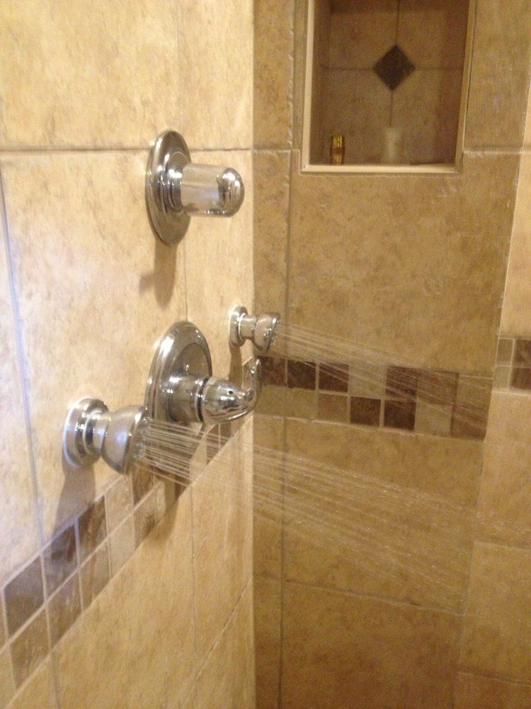 Chrome shower controls and fixtures on beige tiled bathroom wall, with glass shelf niche.