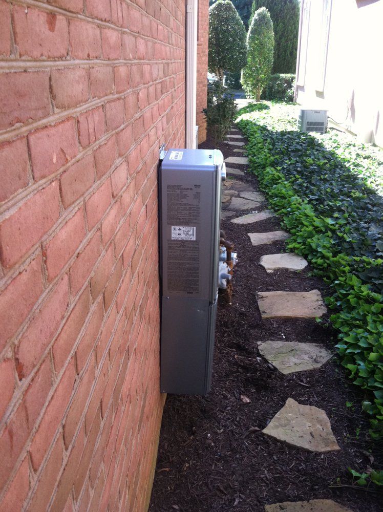 Outdoor HVAC unit beside a red brick wall, next to a narrow garden path with stepping stones.