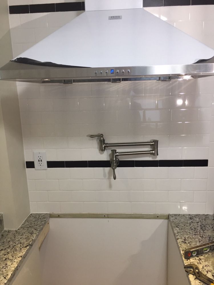 Kitchen wall with white range hood above a faucet over a sink and white tiled backsplash