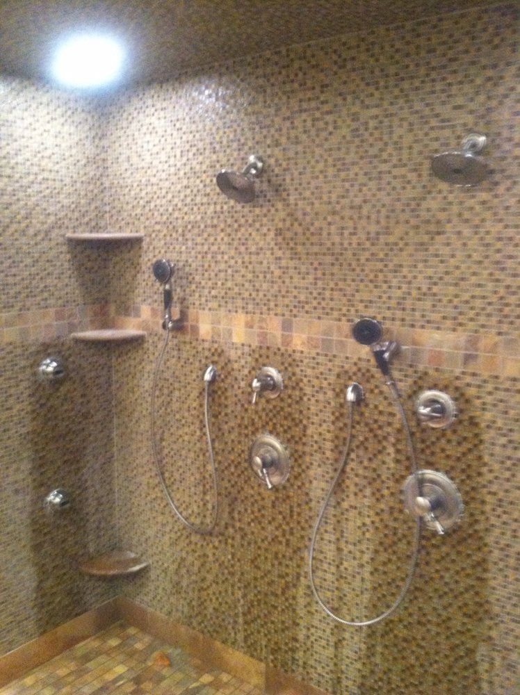 Bathroom shower area with multiple handheld showerheads and beige mosaic tile walls