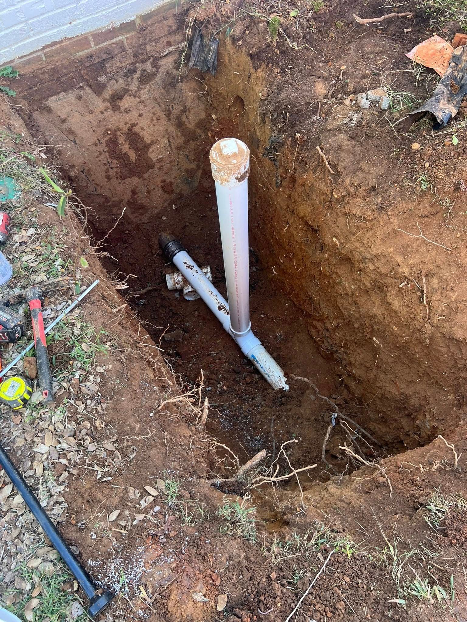 Open trench with exposed white PVC pipe and dirt walls in a grassy yard