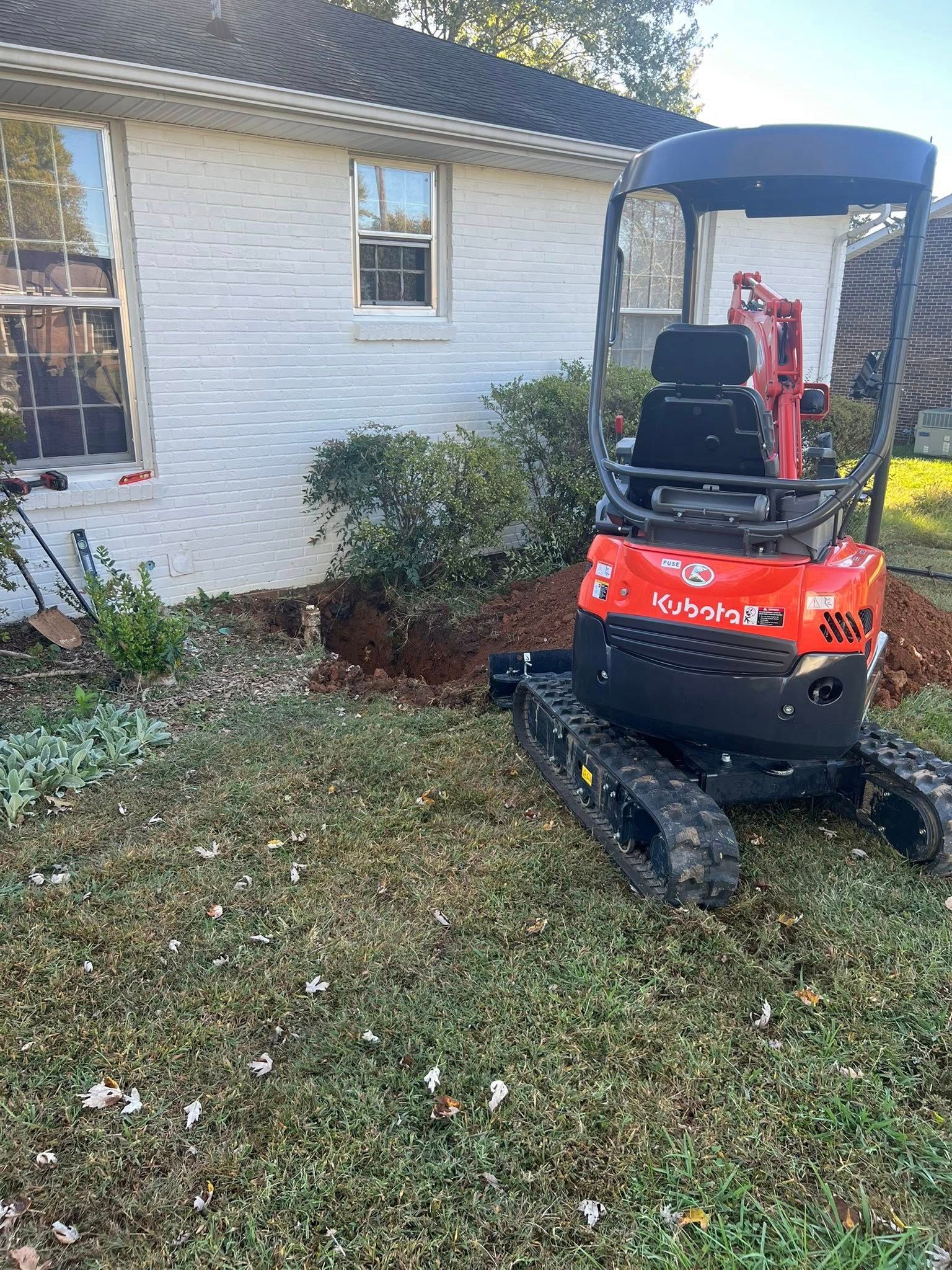 Red mini excavator with a canopy parked beside a white house on a grassy yard.