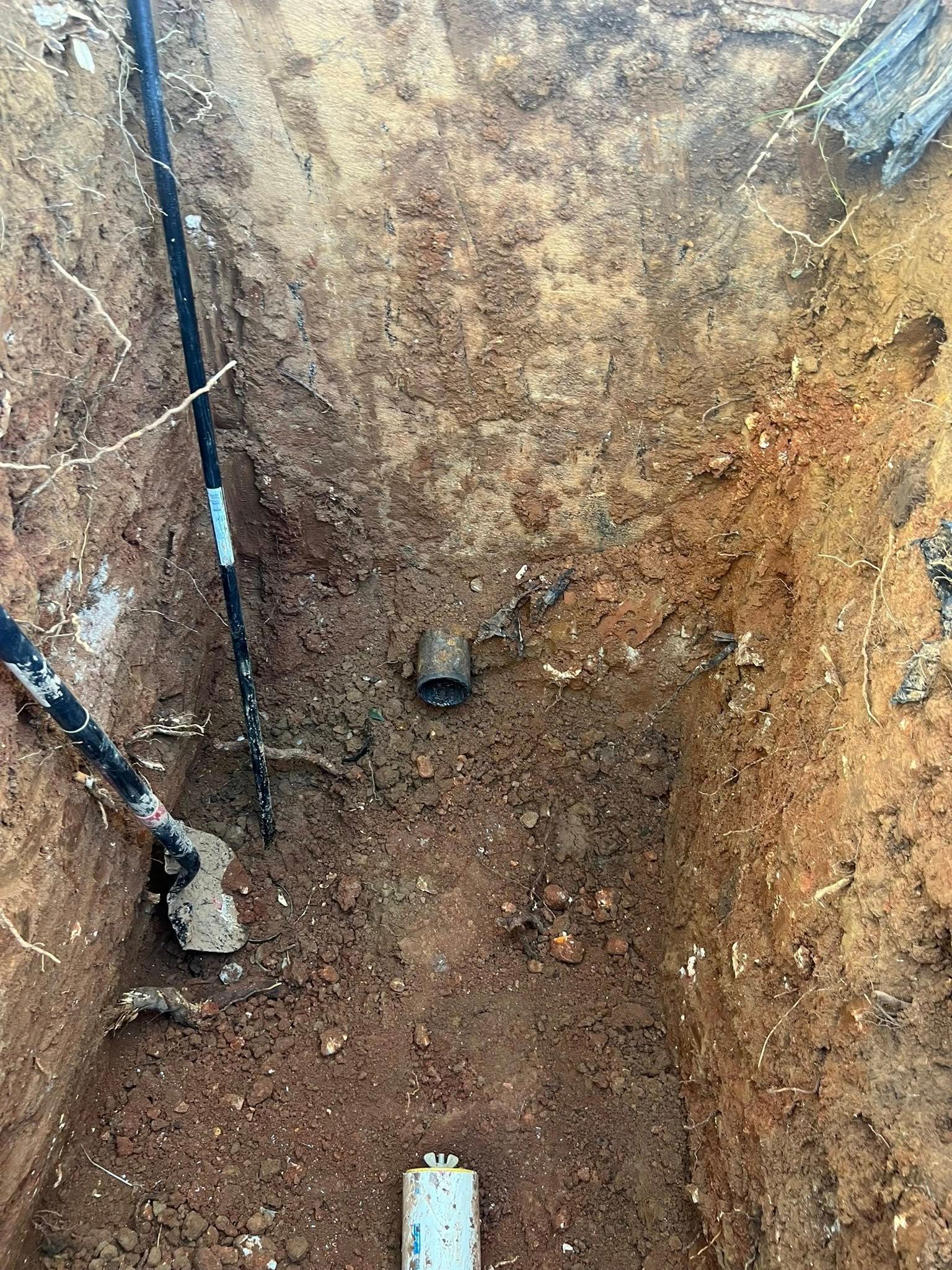 Excavated dirt trench with a small pipe and exposed utility lines along the left wall