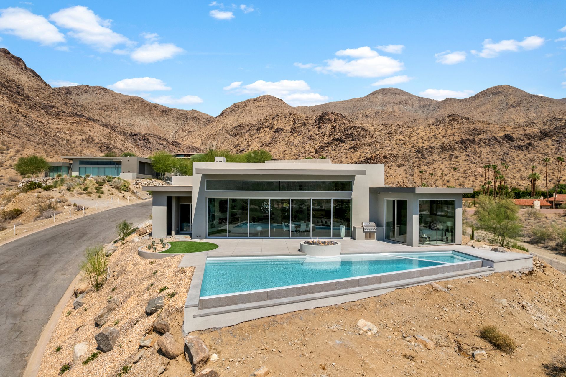 A modern, low-profile house with a rectangular infinity pool overlooking a desert landscape with rugged mountains.