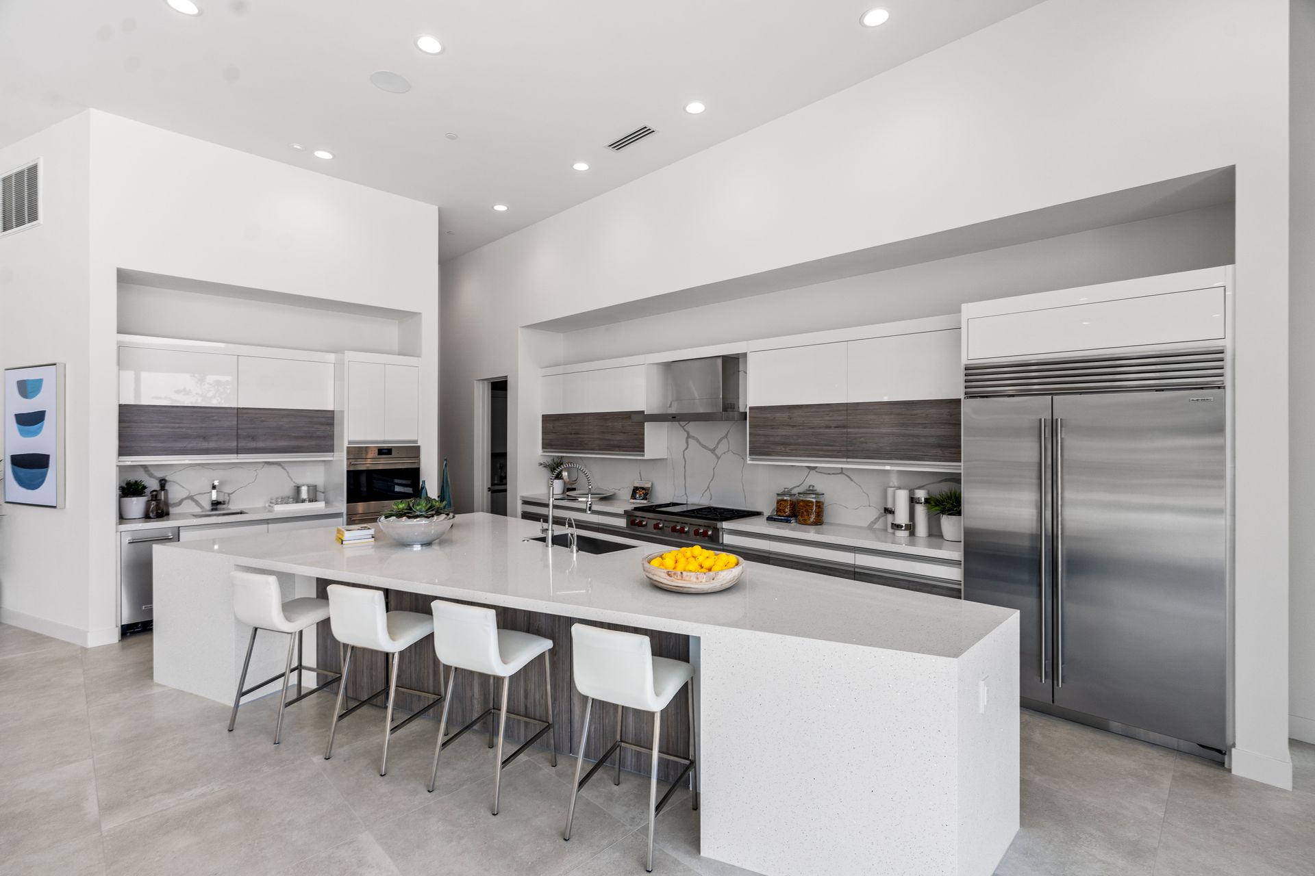 Modern kitchen with white countertops, stainless steel appliances, and four white stools at a large central island.