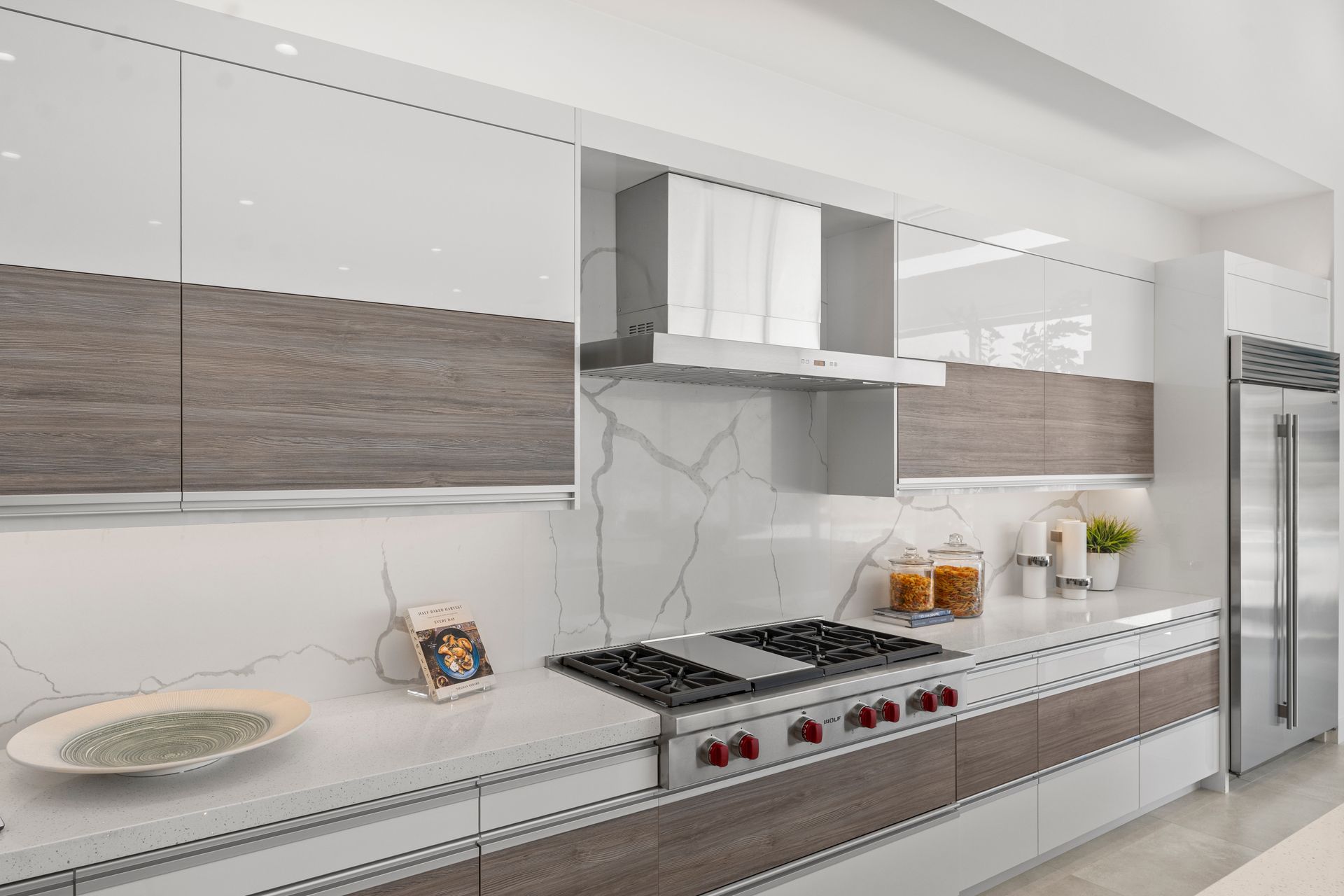 A modern kitchen featuring white and wood-grain cabinets, a marble backsplash, and stainless steel appliances.