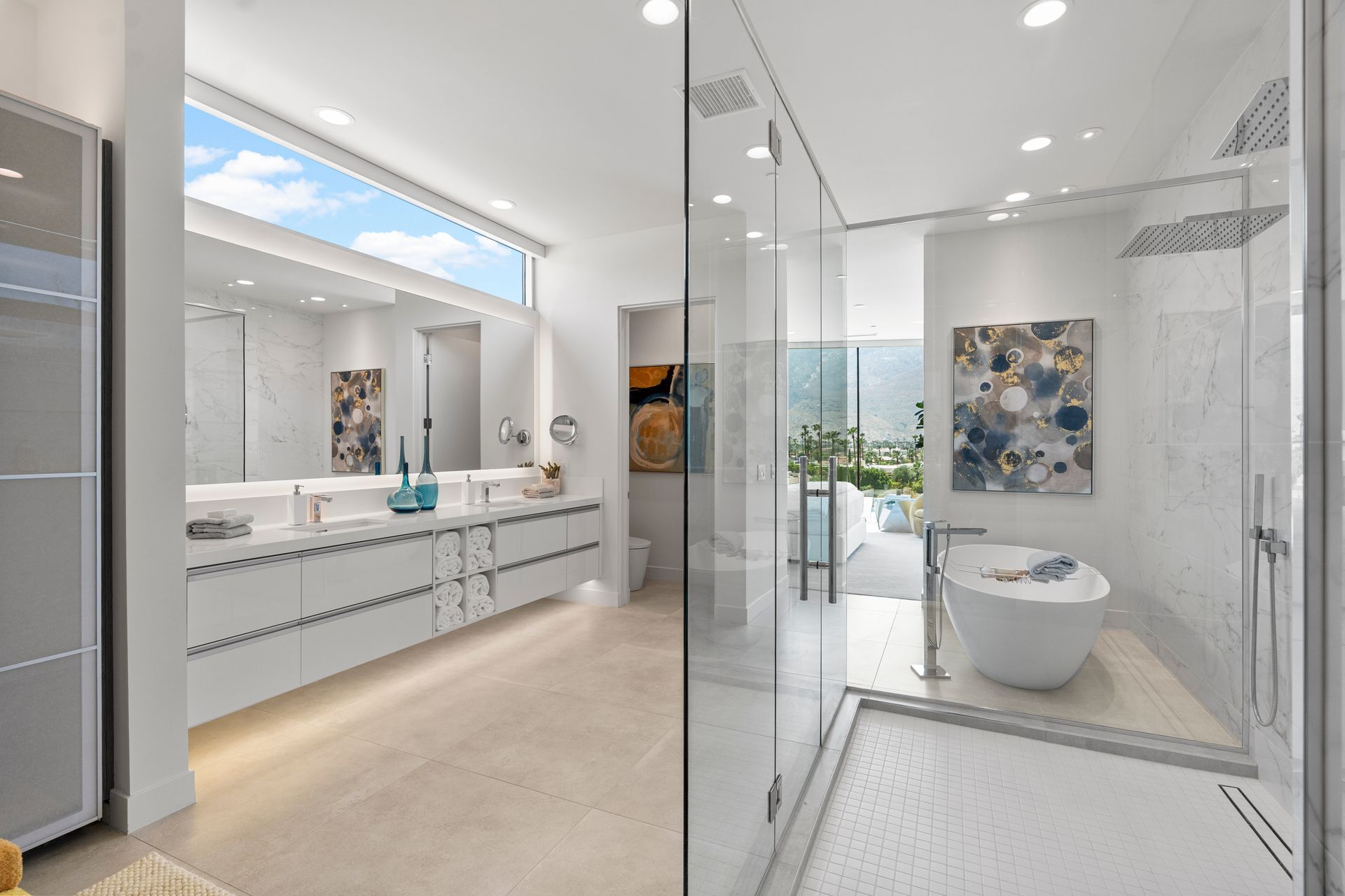Modern white bathroom with double vanity, walk-in glass shower, and a freestanding tub against a marble wall.
