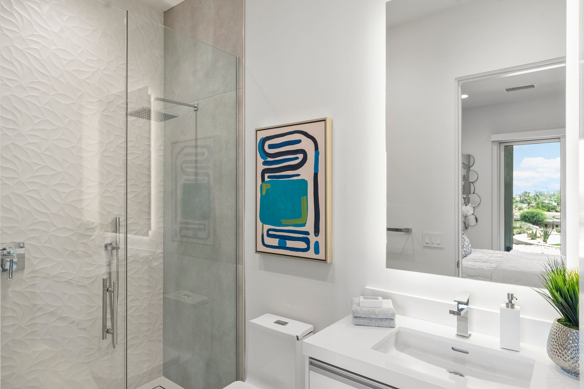 A modern bathroom with a glass-enclosed shower, abstract art on a white wall, and a vanity with a mirror reflecting a room.