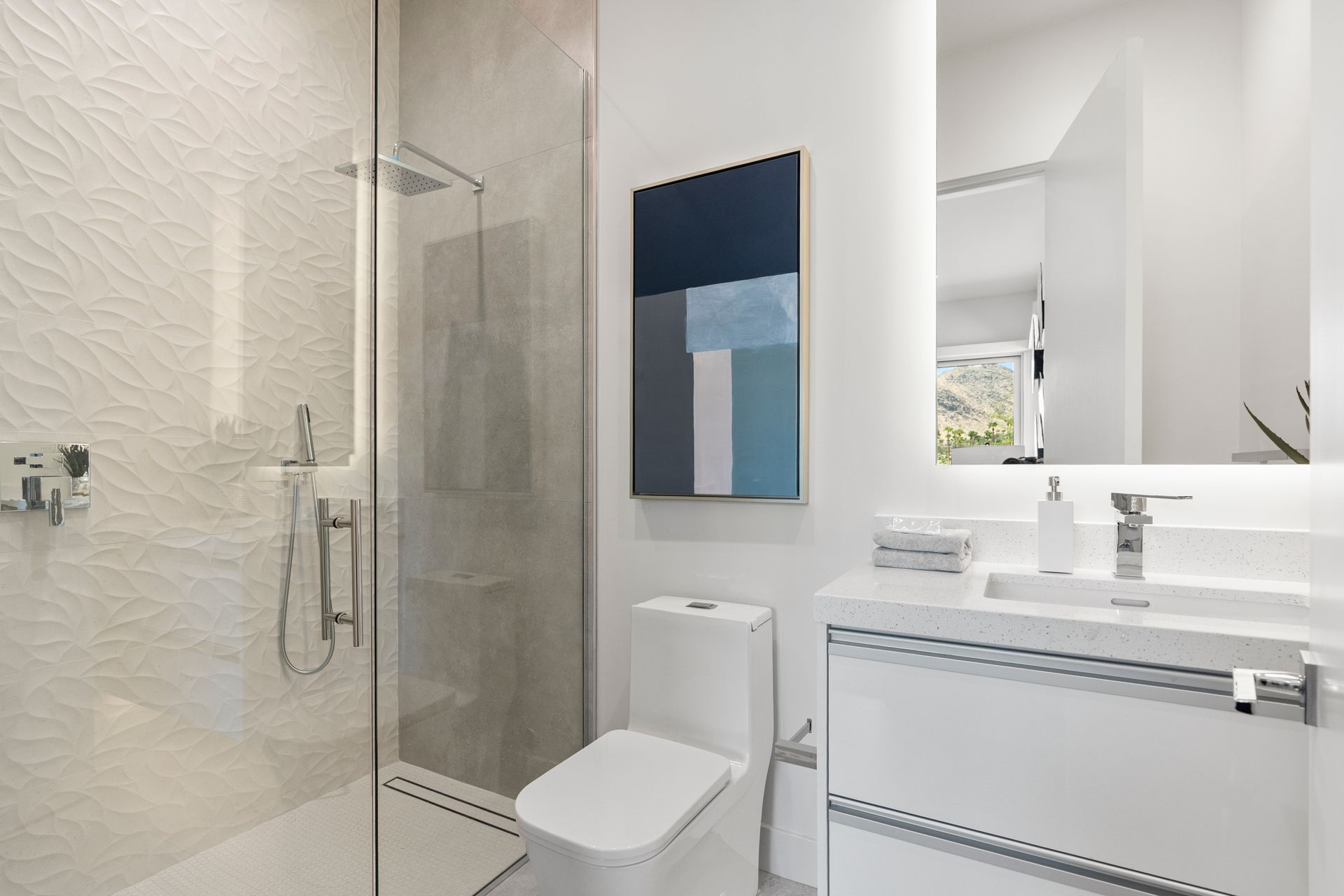 A modern bathroom with a glass-enclosed shower, white toilet, floating vanity, and abstract blue wall art.