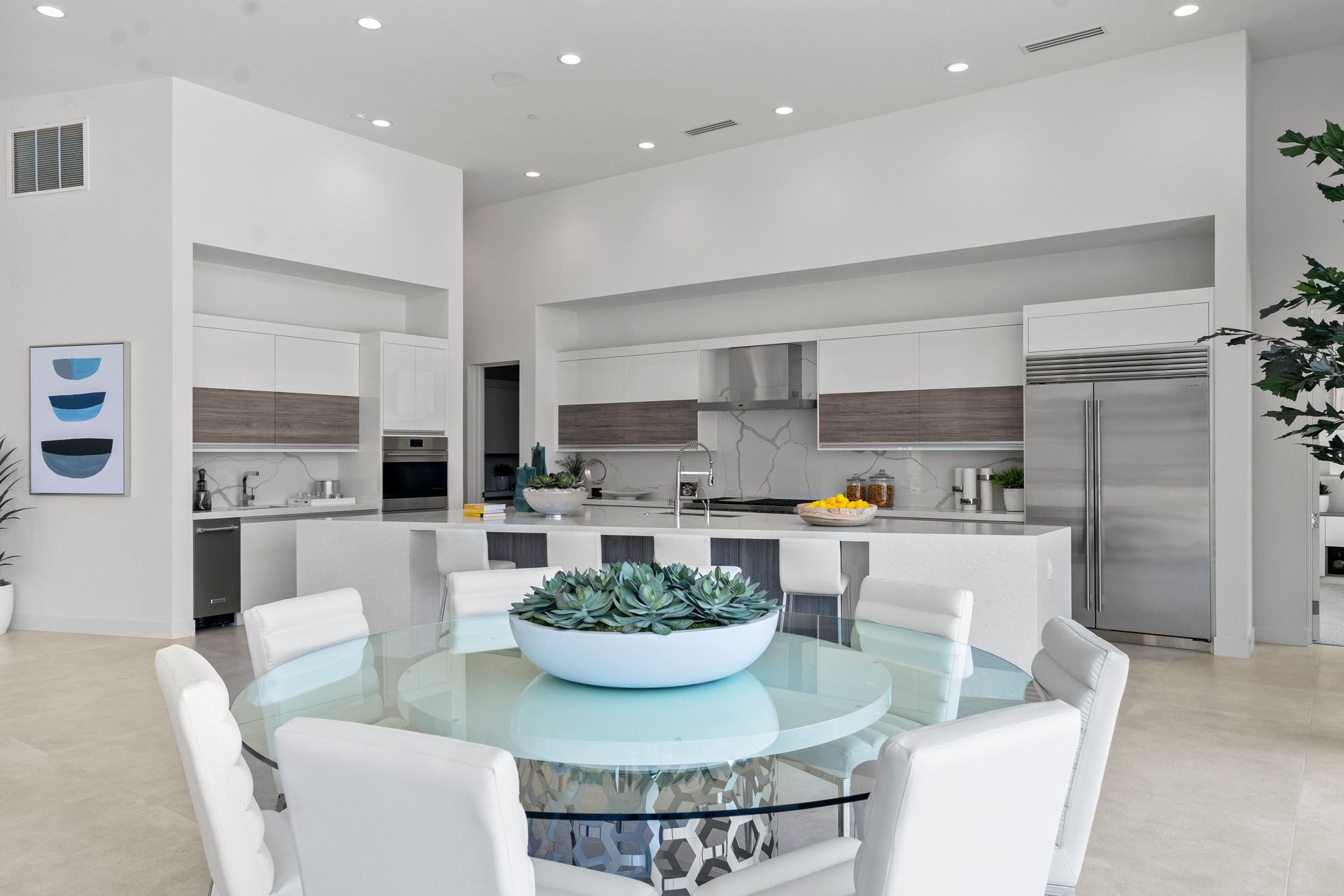 Modern kitchen with white and wood-tone cabinets, a large island, stainless steel appliances, and a glass dining table.
