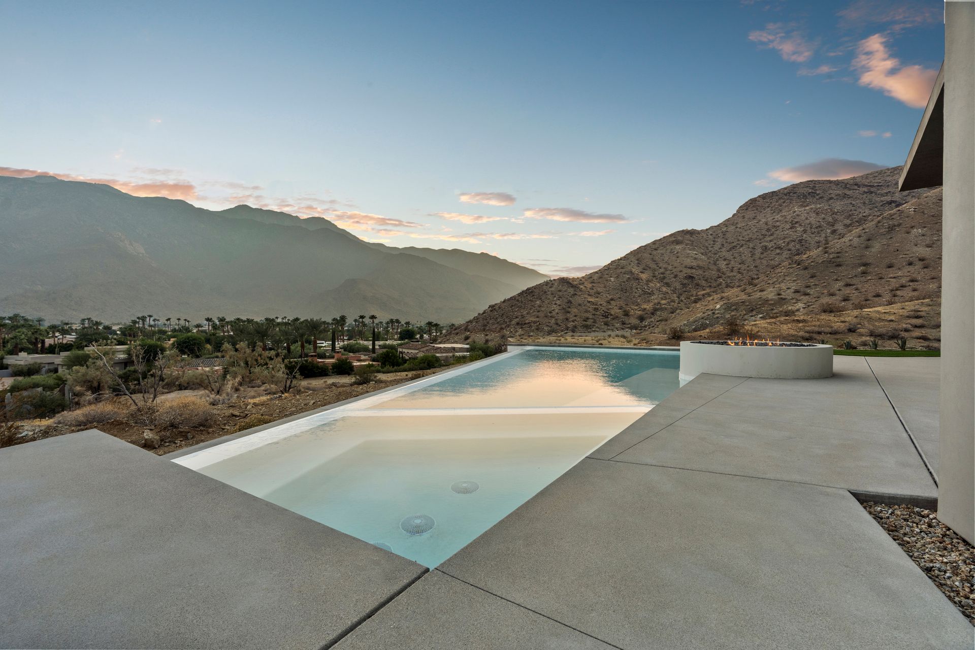 Infinity pool overlooking a desert landscape with mountains in the background at sunset.