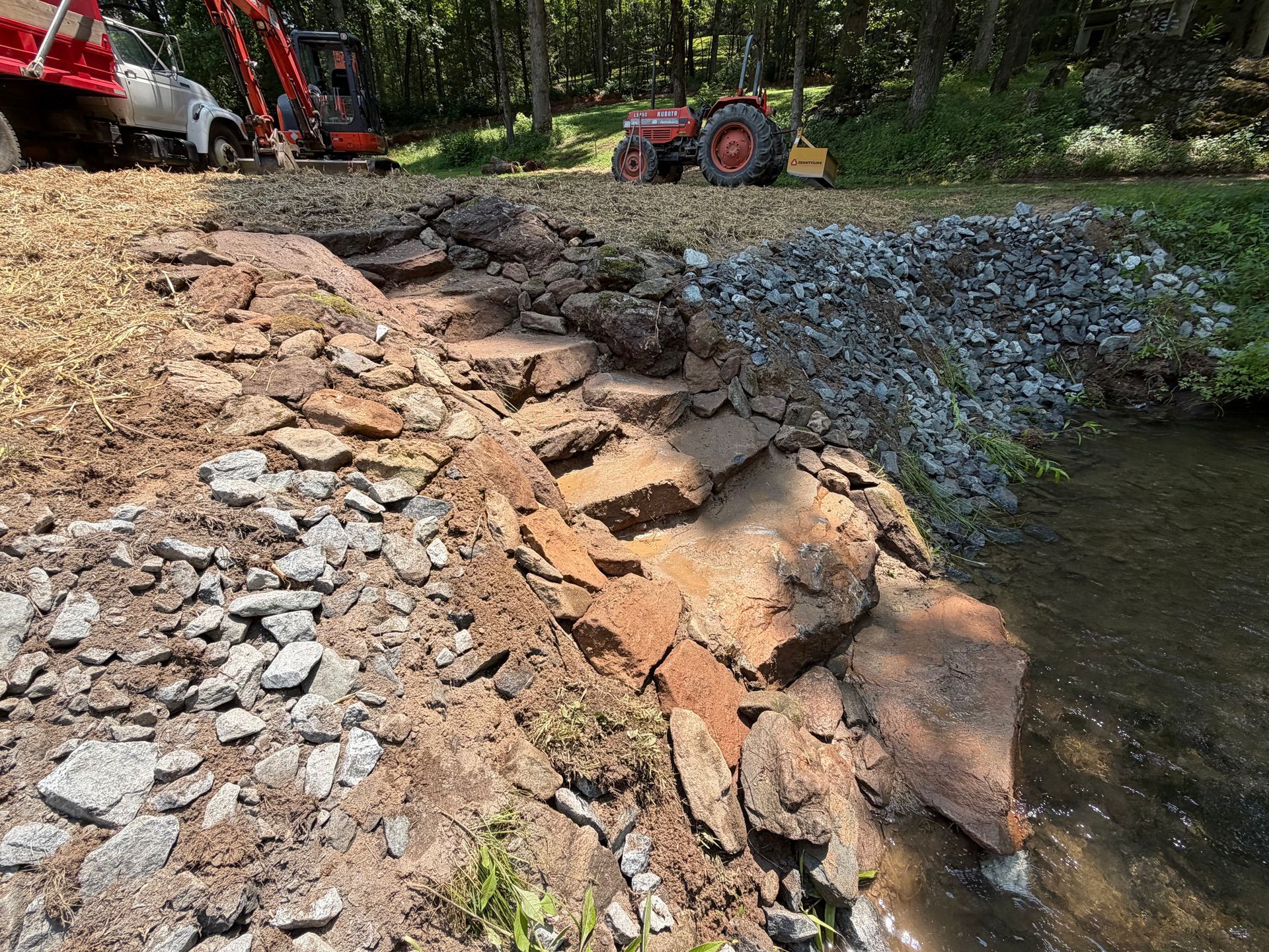 Eroding rocky shoreline with construction machinery repairing the bank beside a pond