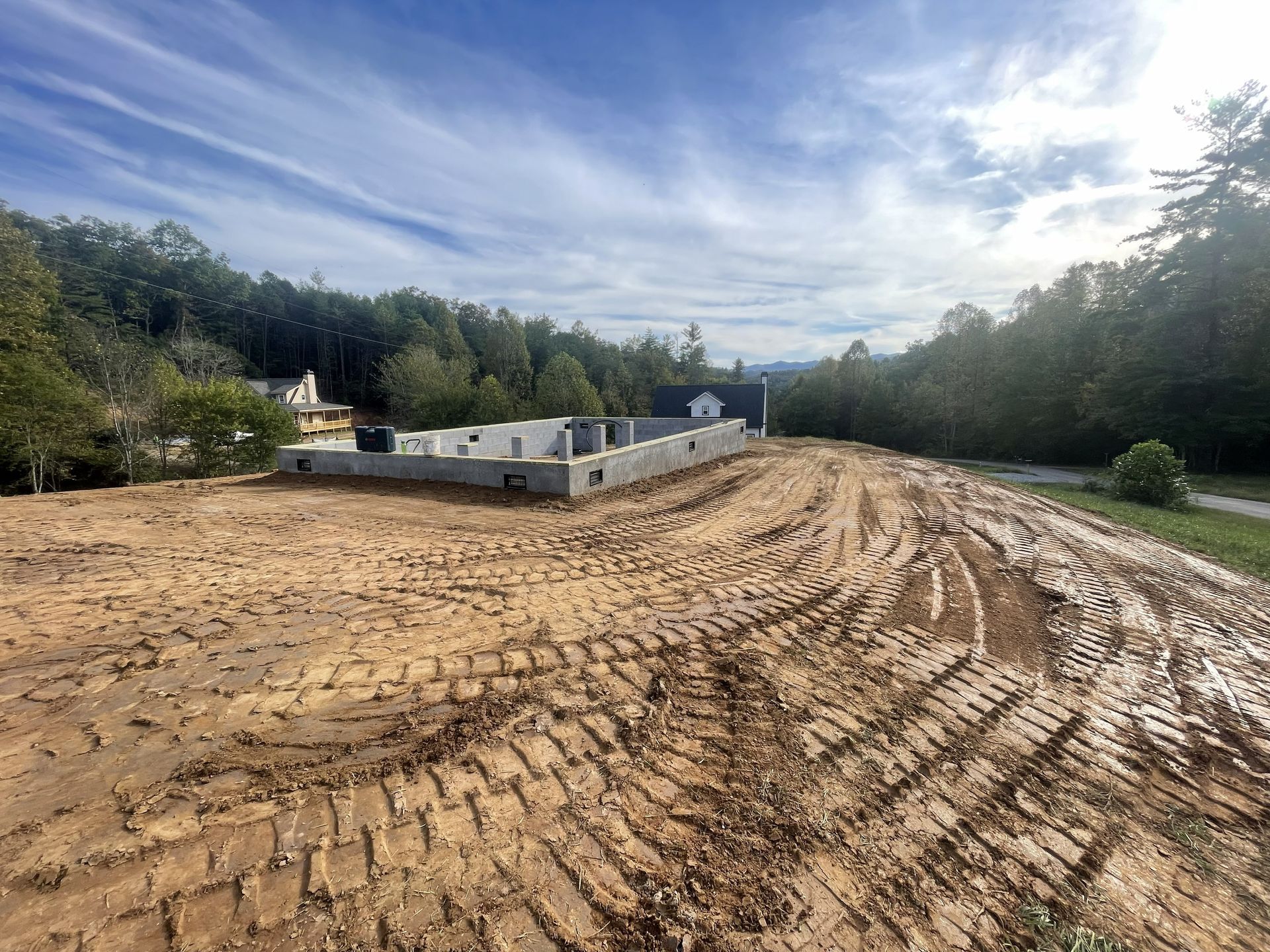 Dirt construction site with graded earth, tire tracks, and portable buildings under a cloudy sky