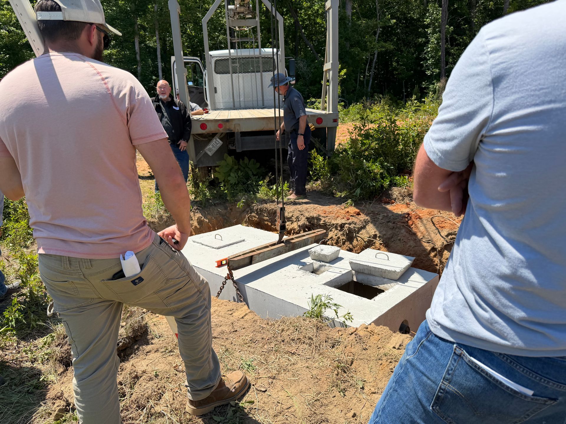 People inspecting concrete utility boxes at a muddy outdoor work site near a truck