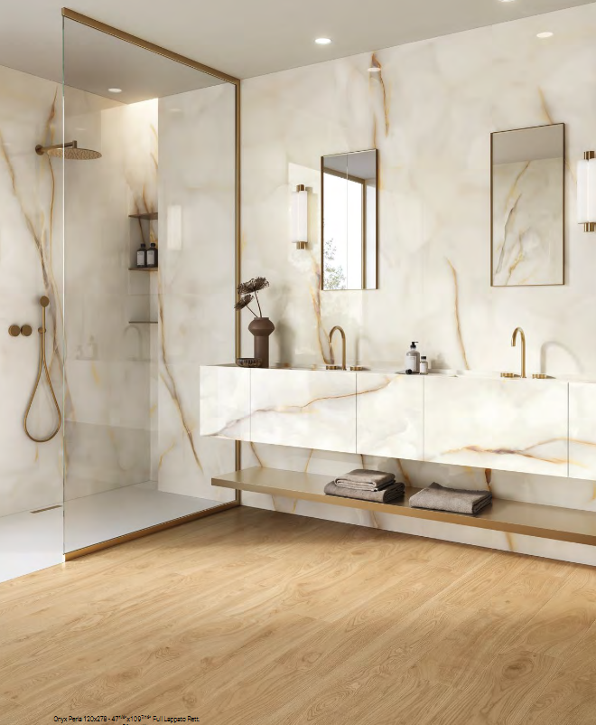 Luxury bathroom with marble walls, brass fixtures, glass shower, and wood floor.