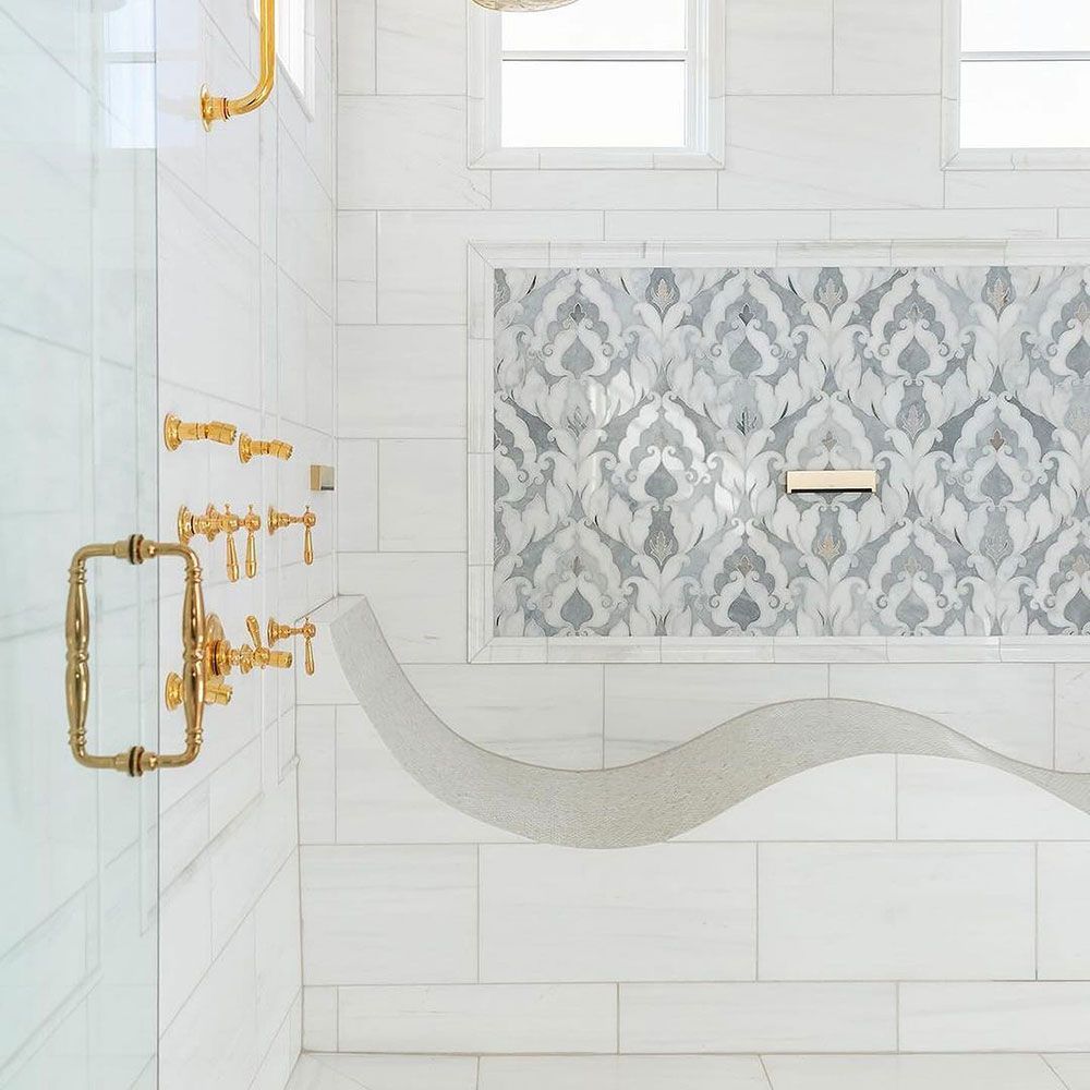 Elegant white marble shower with gold fixtures, patterned tile accent, and curved bench.