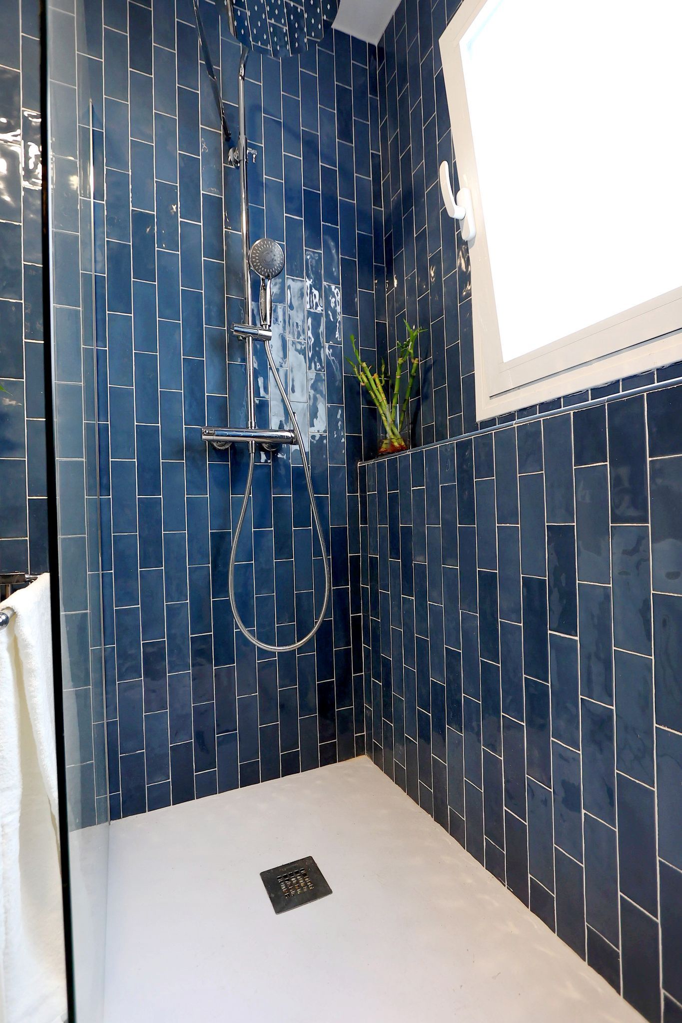 Blue tiled shower with white floor and window.