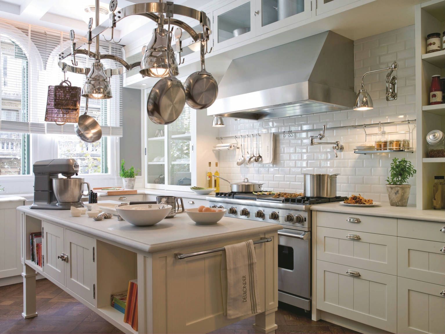 Elegant white kitchen with island, stainless steel appliances, and hanging pots.
