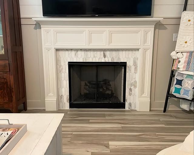 White fireplace with marble tile surround and a black firebox, below a mounted television.