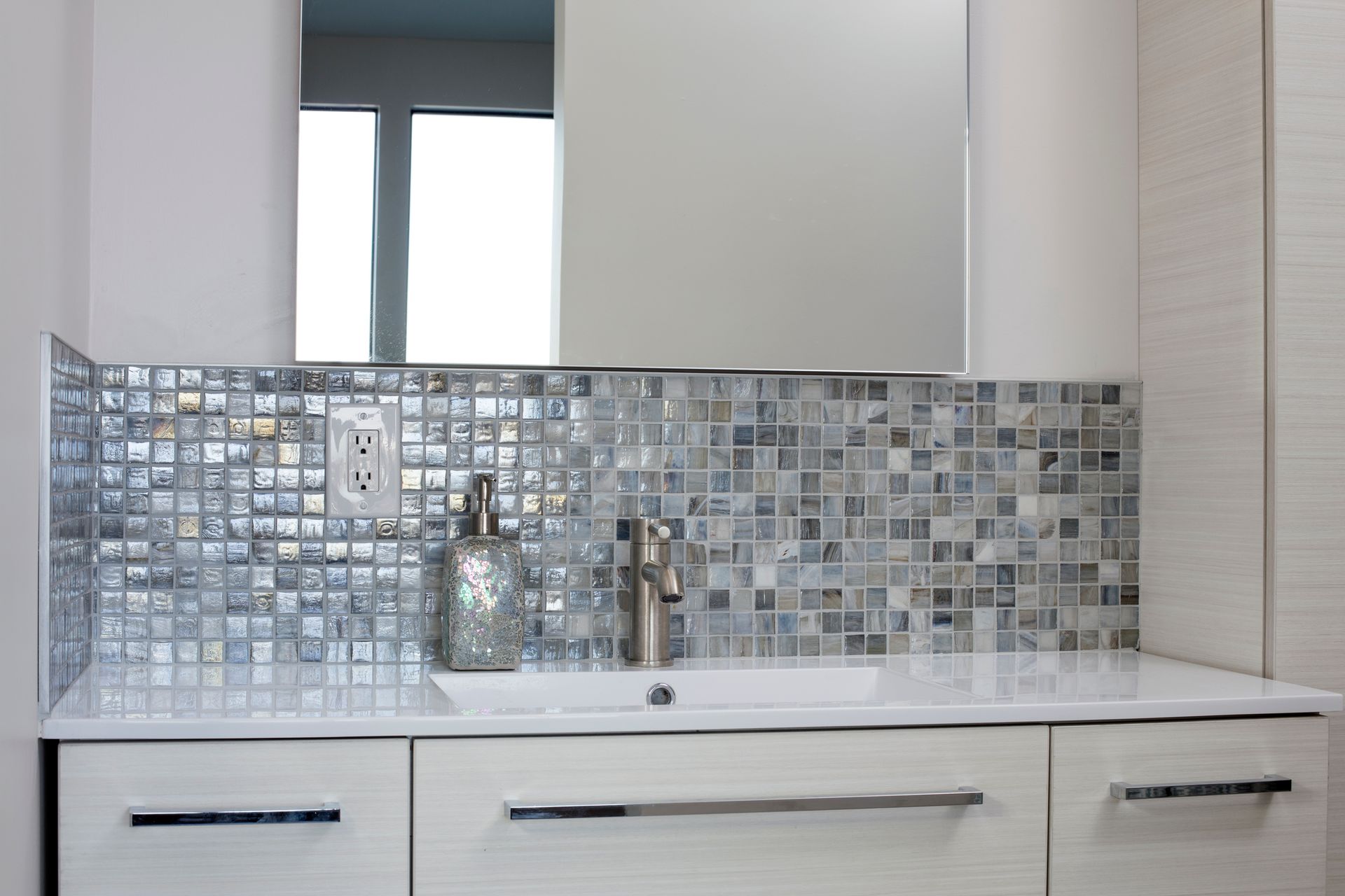 Bathroom vanity with a mosaic tile backsplash and silver fixtures.