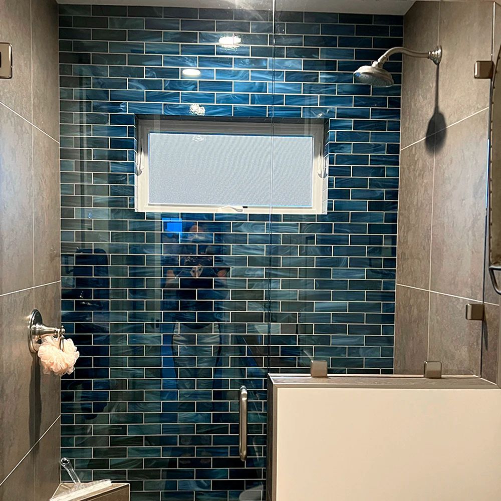 Blue tiled shower with glass enclosure, gray walls, and a window.