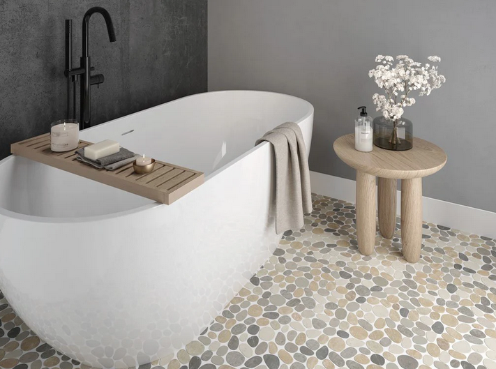 Bathroom with a white freestanding tub, pebble tile floor, and a small wooden side table.
