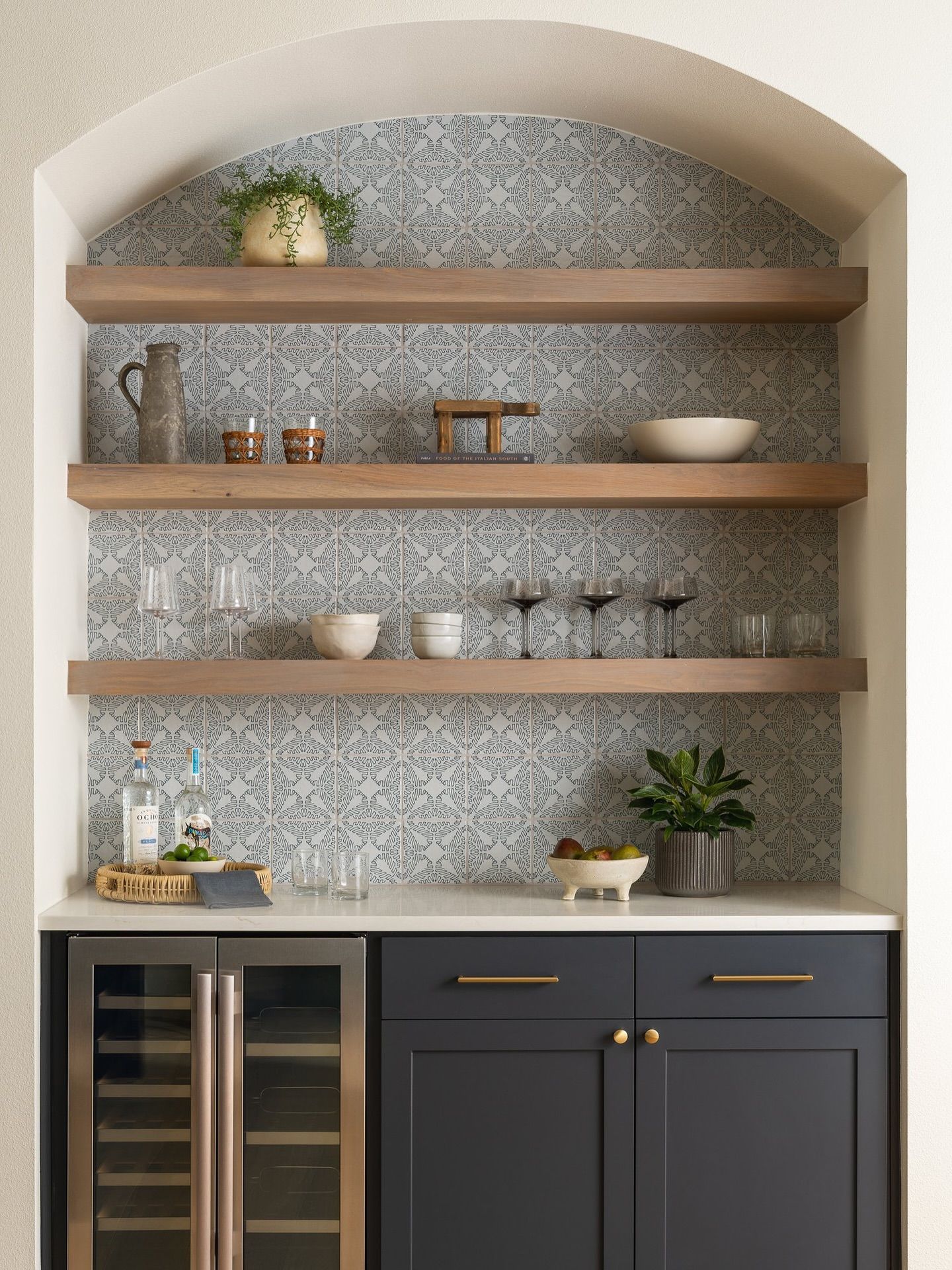 Built-in bar with shelves, dark blue cabinets, marble countertop, and mosaic tile backsplash.