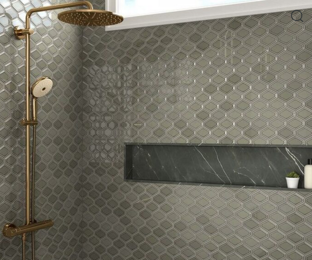 Shower with gray scale tile walls, gold fixtures, and a shelf with toiletries.