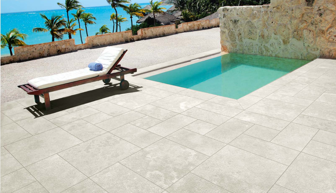 Lounge chair by a pool with ocean view. Light-colored patio tiles.