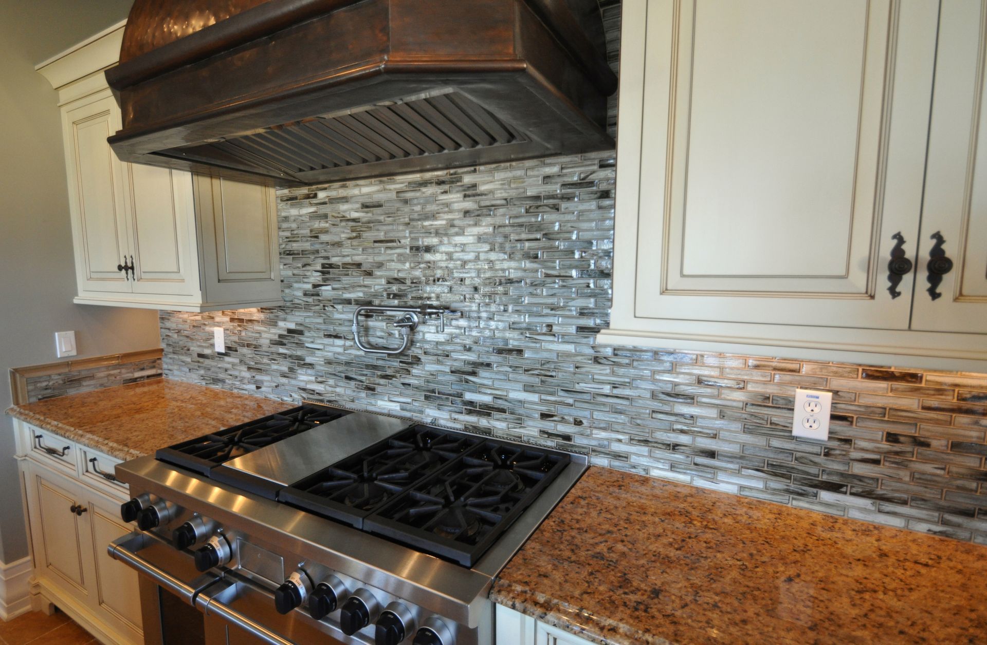 Kitchen with stainless steel range, copper hood, granite counters, and mosaic tile backsplash.